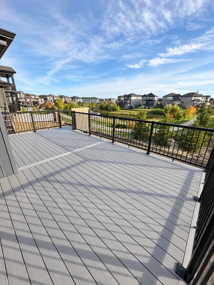 Grey composite deck with picture-frame border and black aluminum railing overlooking a pond, Edmonton — TrueBlue Builders Ltd